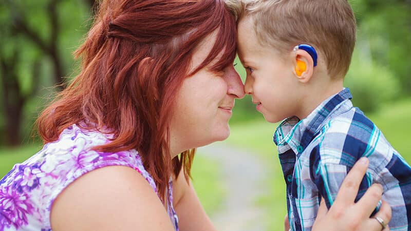A mother looking into her child's eyes. Child has a hearing aid.